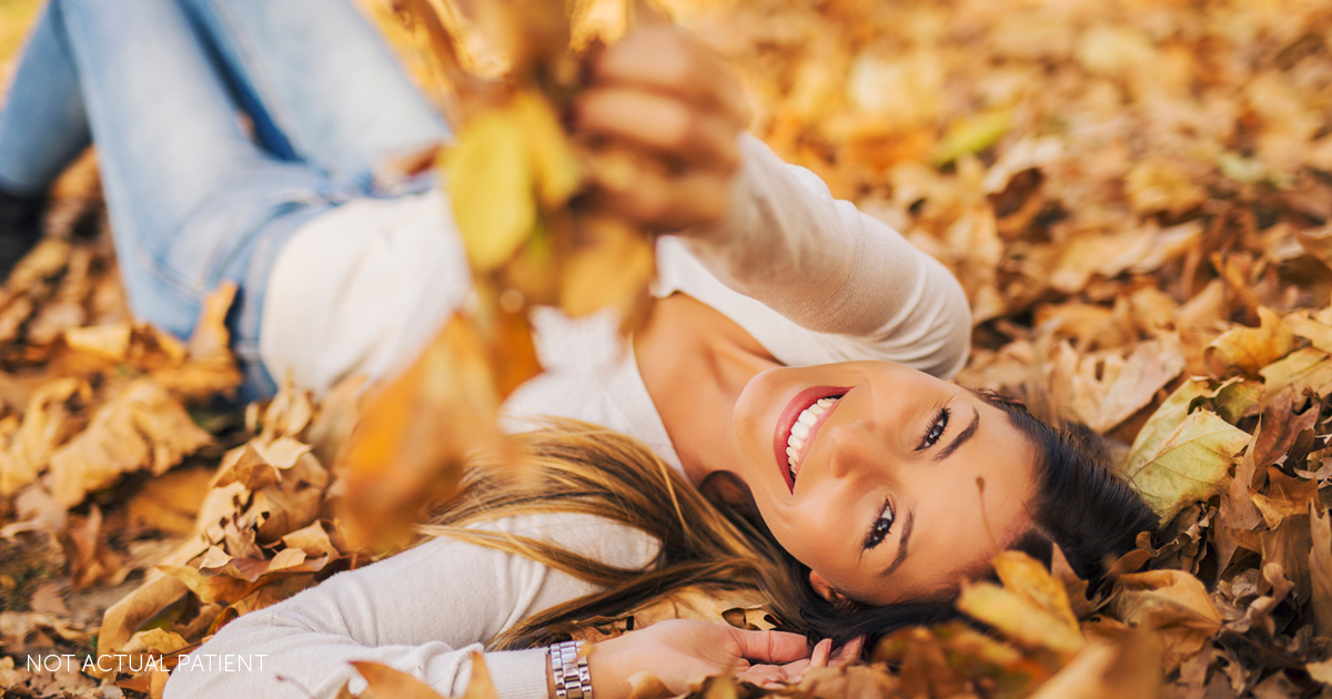 brunette woman smiling and laying down in leaves