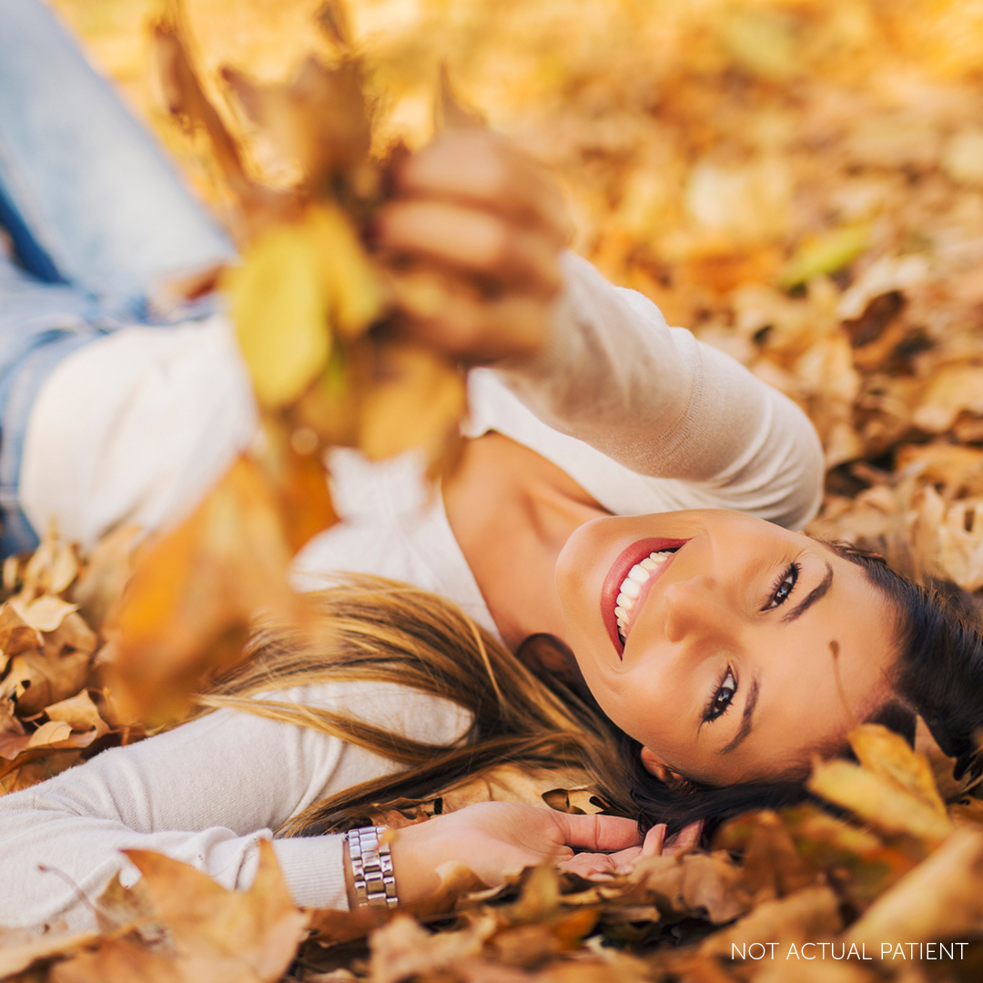 brunette woman smiling and laying down in leaves