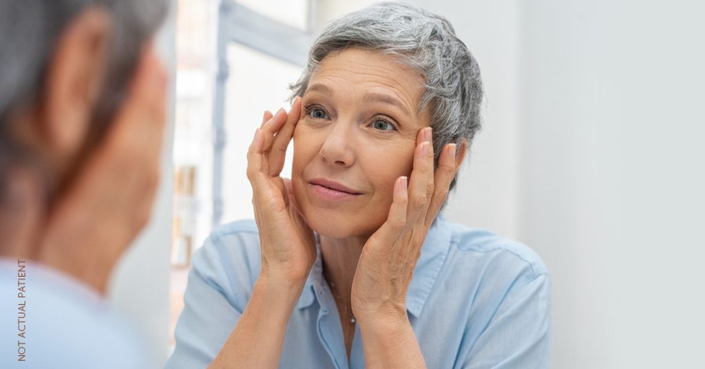 Woman standing in front of a mirror looking at her face (not actual patient)