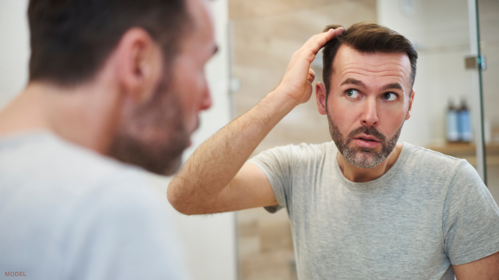 Man looking in mirror touching hair (model)