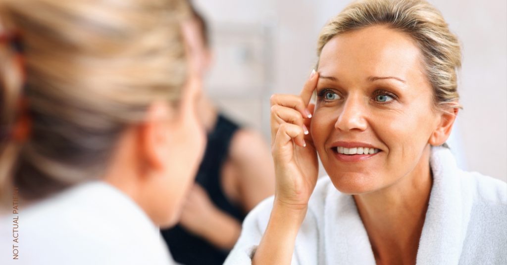 Woman looking in mirror lifting eyebrow (model)