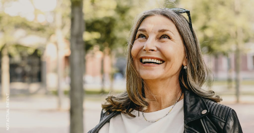 A beautiful middle-aged woman is looking up and laughing as she stands outside. (model)