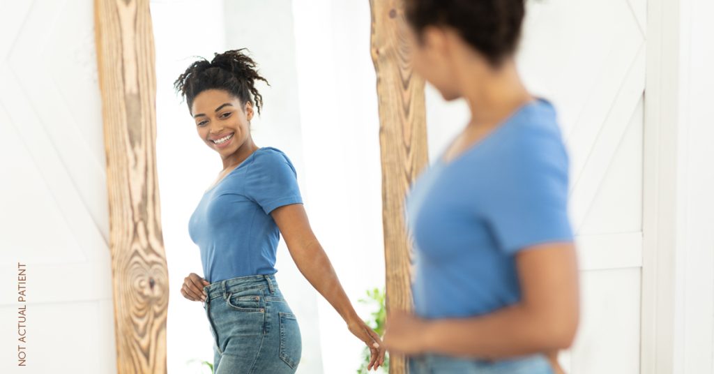 Young woman looking at how her jeans fit in the mirror. (model)