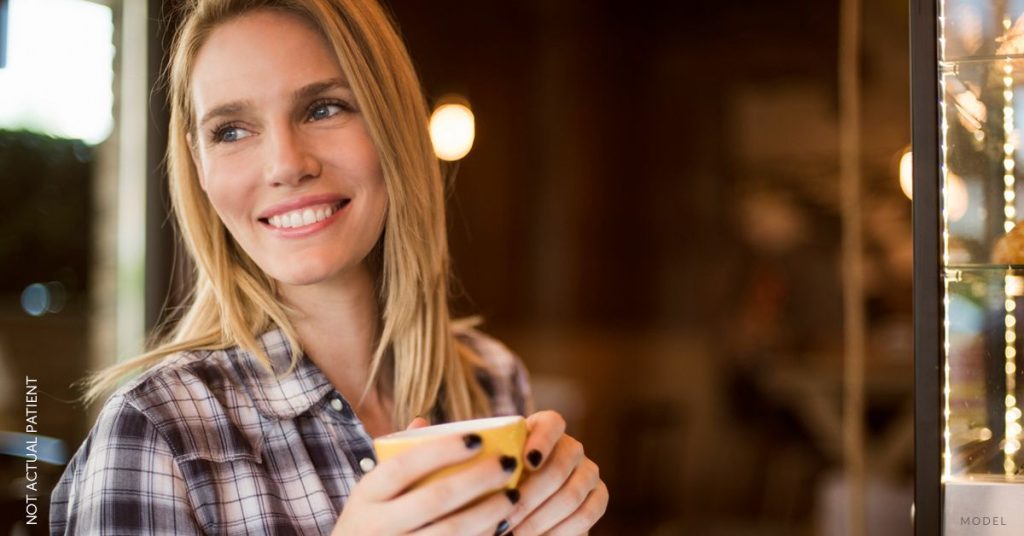 A beautiful woman (NOT REAL PATIENT) in a plaid shirt holding a cup of coffee and smiling while looking off into the distance. (MODEL)
