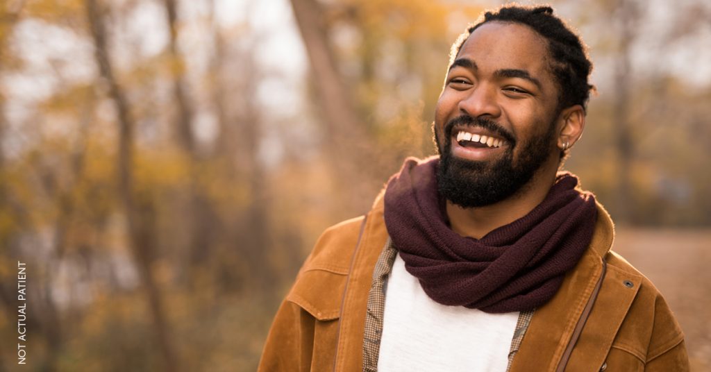 Handsome man in scarf and other fall attire is standing outside on a fall day and laughing at something of camera. (Model)