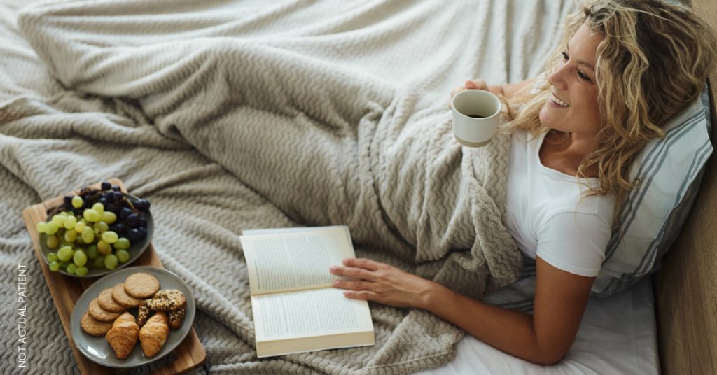 Young woman lying in bed, reading a book (model)