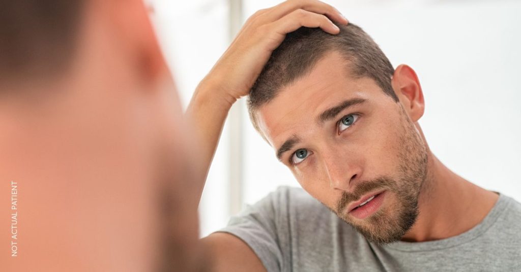 Man looking in the mirror touching his hair. (MODEL)