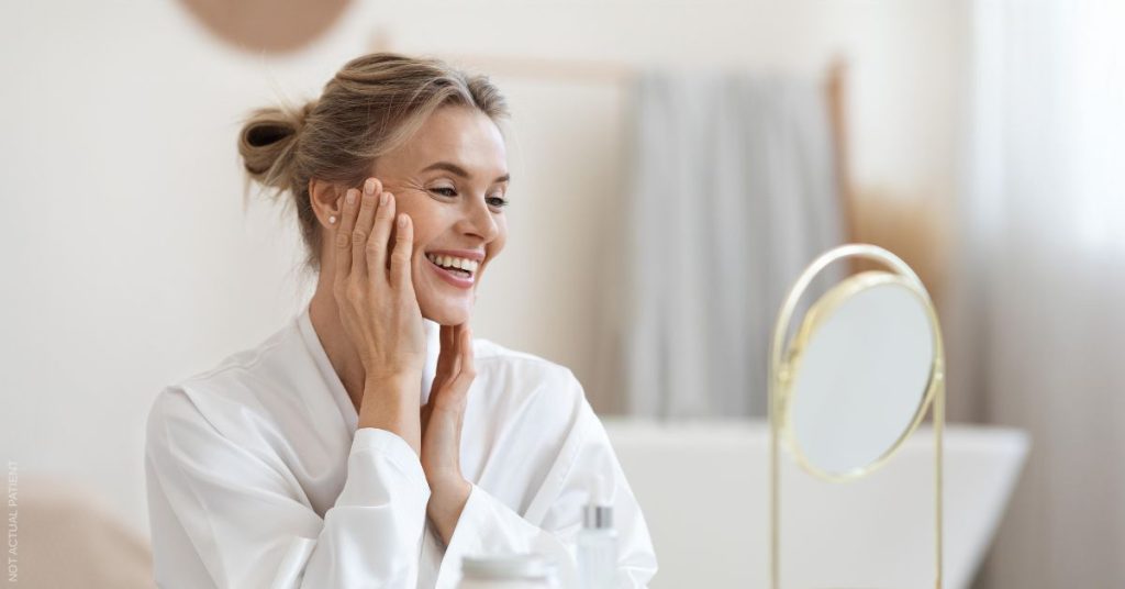 Woman looking in the mirror after facelift procedure (not actual patient)