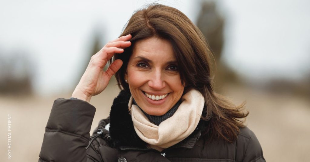 Smiling woman outdoors, brushing hair back from her face and eyes (model)